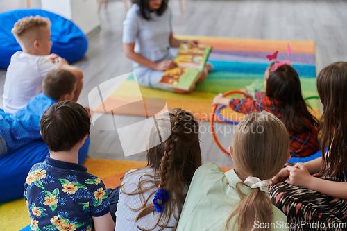 Image of Reading time in an elementary school or kindergarten, a teacher reading a book to children in an elementary school or kindergarten. The concept of pre-school education. Selective focus