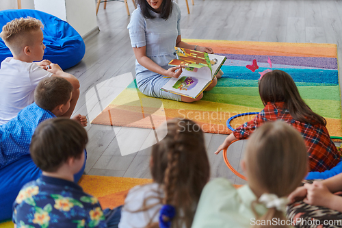 Image of Reading time in an elementary school or kindergarten, a teacher reading a book to children in an elementary school or kindergarten. The concept of pre-school education. Selective focus