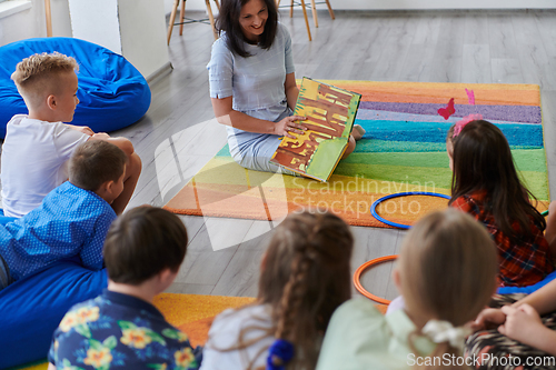 Image of Reading time in an elementary school or kindergarten, a teacher reading a book to children in an elementary school or kindergarten. The concept of pre-school education. Selective focus