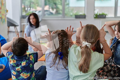 Image of A happy female teacher sitting and playing hand games with a group of little schoolchildren