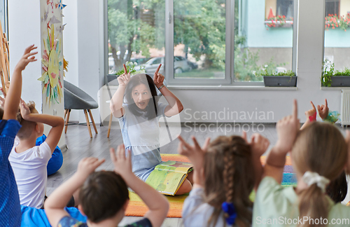 Image of A happy female teacher sitting and playing hand games with a group of little schoolchildren