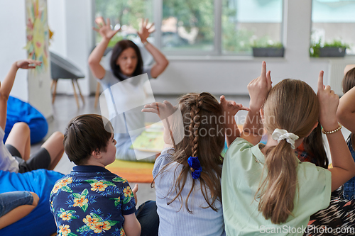 Image of A happy female teacher sitting and playing hand games with a group of little schoolchildren