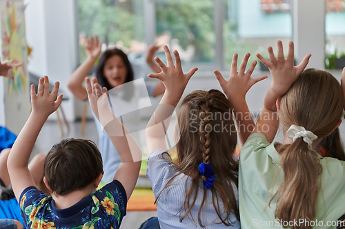 Image of A happy female teacher sitting and playing hand games with a group of little schoolchildren