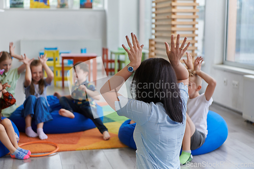 Image of A happy female teacher sitting and playing hand games with a group of little schoolchildren