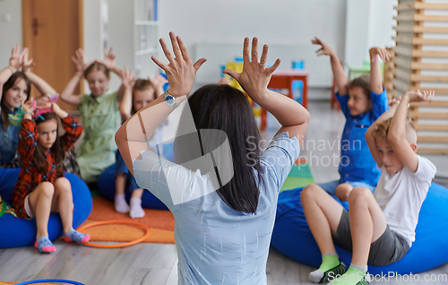 Image of A happy female teacher sitting and playing hand games with a group of little schoolchildren