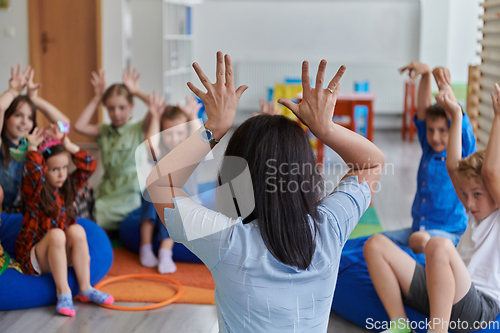 Image of A happy female teacher sitting and playing hand games with a group of little schoolchildren