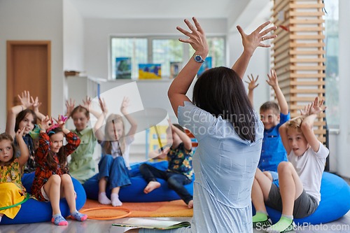 Image of A happy female teacher sitting and playing hand games with a group of little schoolchildren