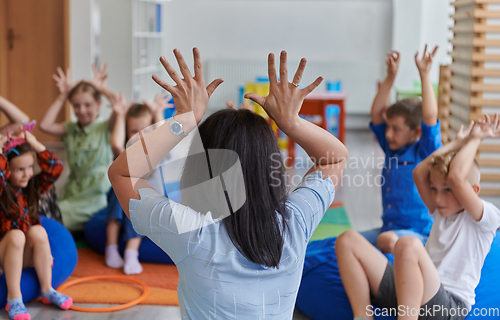 Image of A happy female teacher sitting and playing hand games with a group of little schoolchildren