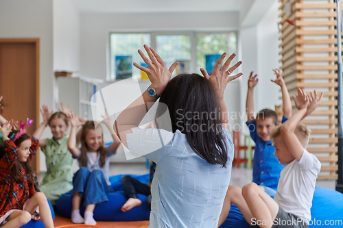 Image of A happy female teacher sitting and playing hand games with a group of little schoolchildren