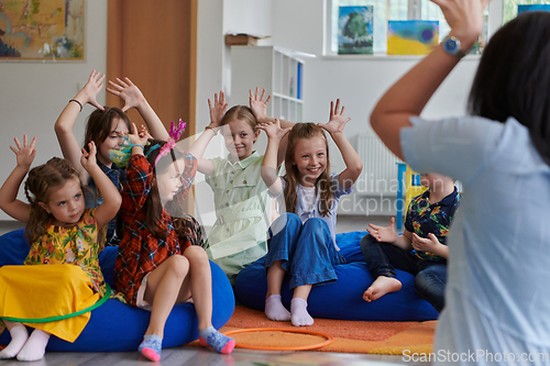 Image of A happy female teacher sitting and playing hand games with a group of little schoolchildren