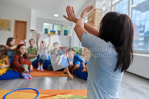 Image of A happy female teacher sitting and playing hand games with a group of little schoolchildren