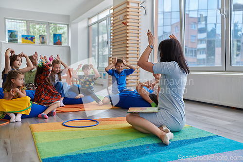 Image of A happy female teacher sitting and playing hand games with a group of little schoolchildren