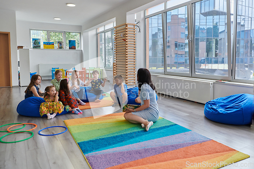 Image of Reading time in an elementary school or kindergarten, a teacher reads a book to children in an elementary school or kindergarten. The concept of pre-school education. Selective focus