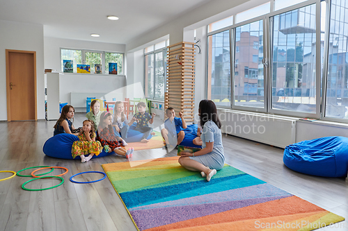 Image of Reading time in an elementary school or kindergarten, a teacher reads a book to children in an elementary school or kindergarten. The concept of pre-school education. Selective focus