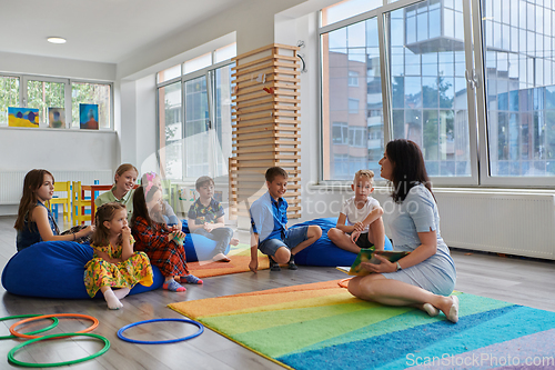 Image of Reading time in an elementary school or kindergarten, a teacher reads a book to children in an elementary school or kindergarten. The concept of pre-school education. Selective focus