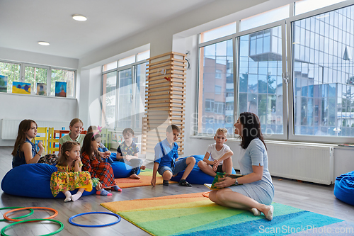 Image of Reading time in an elementary school or kindergarten, a teacher reads a book to children in an elementary school or kindergarten. The concept of pre-school education. Selective focus