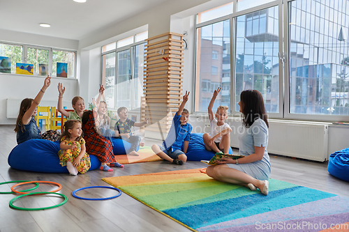 Image of Reading time in an elementary school or kindergarten, a teacher reads a book to children in an elementary school or kindergarten. The concept of pre-school education. Selective focus