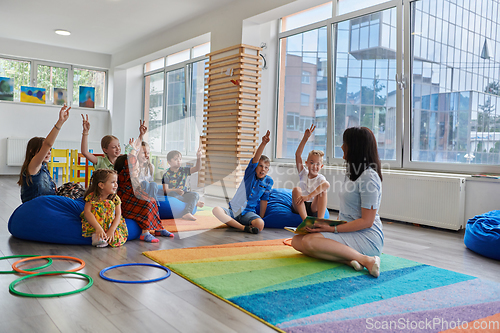 Image of Reading time in an elementary school or kindergarten, a teacher reads a book to children in an elementary school or kindergarten. The concept of pre-school education. Selective focus