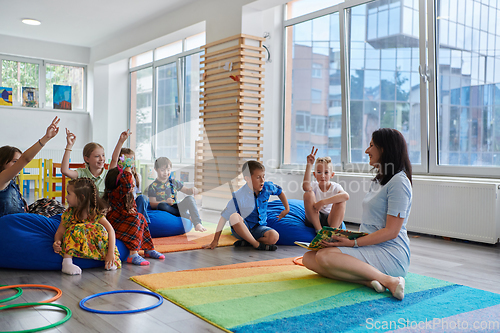 Image of Reading time in an elementary school or kindergarten, a teacher reads a book to children in an elementary school or kindergarten. The concept of pre-school education. Selective focus