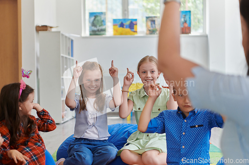 Image of A happy female teacher sitting and playing hand games with a group of little schoolchildren