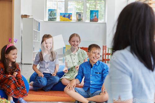 Image of A happy female teacher sitting and playing hand games with a group of little schoolchildren