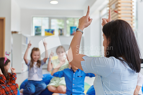 Image of A happy female teacher sitting and playing hand games with a group of little schoolchildren