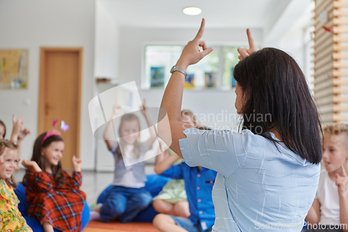 Image of A happy female teacher sitting and playing hand games with a group of little schoolchildren