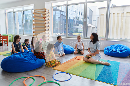 Image of Reading time in an elementary school or kindergarten, a teacher reads a book to children in an elementary school or kindergarten. The concept of pre-school education. Selective focus