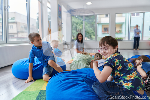 Image of A happy female teacher sitting and playing hand games with a group of little schoolchildren