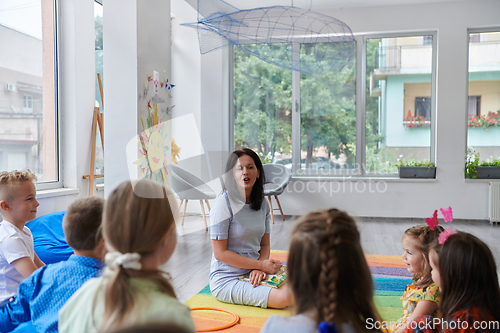 Image of A happy female teacher sitting and playing hand games with a group of little schoolchildren