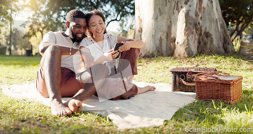 Image of Happy, social media and an interracial couple on a picnic with a phone for communication, tech or an app. Talking, summer and a black man and woman with a mobile for a chat on a date in a park