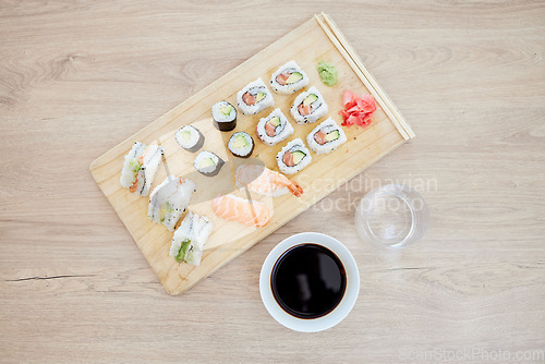 Image of Sushi, top view and soy sauce with seafood on wood board, closeup with salmon and rice, healthy and luxury. Japanese cuisine, catering with lunch or dinner meal, chopsticks and food with nutrition