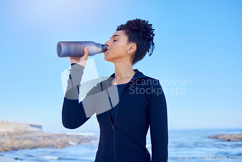 Image of Fitness, woman and drinking water at beach for running, health or morning cardio on blue sky by an ocean. Exercise, hydration and thirsty lady runner with sports liquid after training or sea workout