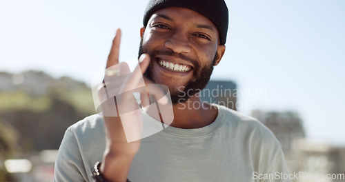 Image of Hand, happy and sign with a black man showing a gesture while standing outdoor in the city with a smile on his face. Portrait, freedom and carefree with a young male gesturing or signing in a town