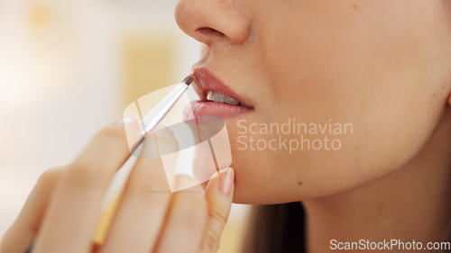 Image of Painting young woman with pink lipstick on her mouth with brush, makes a kissing movement with lips and with a smile of excitement. Beauty products, cosmetics and makeup are part of female self care
