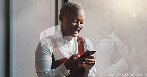 Image of Happy, smile and face of a black woman on a phone while standing by the window in office. Technology, happiness and African female employee networking on social media or the internet on break at work