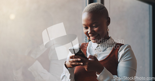 Image of Happy, smile and face of a black woman on a phone while standing by the window in office. Technology, happiness and African female employee networking on social media or the internet on break at work