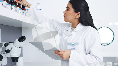 Image of Medical researcher checking bottles with chemicals inside a modern science lab. Young focused scientist or pharmacist looking at hazardous and dangerous inventory while writing notes in a pharmacy