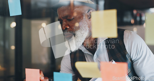 Image of Strategy, planning and black man with sticky notes on glass wall brainstorming for new project. Development, motivation and small business startup at at night, man thinking and writing notes for idea