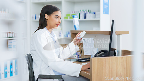 Image of Young pharmacist working on computer at a pharmacy counter. Woman using technology to access drug database, does inventory checkup and dispensing online medicine prescriptions in a drugstore