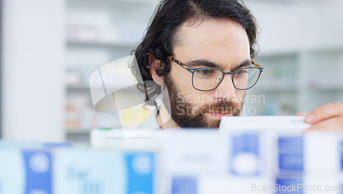 Image of Man with glasses choosing medication on a shelf in a pharmacy. Customer with glasses browsing in aisle in a drugstore and finding what he needs before heading to the checkout with his vitamins