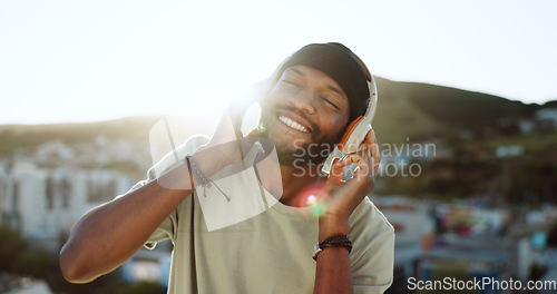 Image of Man, music and dancing on rooftop with headphones in sunshine, city and summer with smile. Happy, black man and streaming to listen on internet, web or app to relax, dance and radio in Cape Town