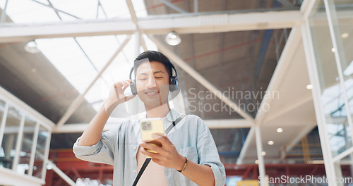 Image of Phone, music headphones and Asian man walking in mall streaming podcast or radio. Technology, travel and happy male listening to song, audio sound or playlist on mobile smartphone in urban building.