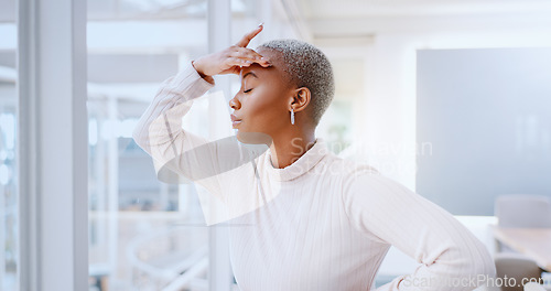 Image of Young african american business woman suffering from a headache while standing in her office alone at work. Stressed black female business person looking tired while putting in overtime late at night