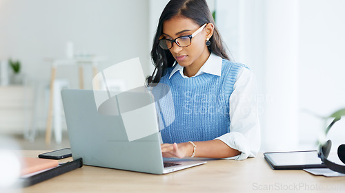 Image of Young woman happily doing business and networking by email on laptop. Professional female is stylish and creative while being alone in office. She is using technology to advance her career