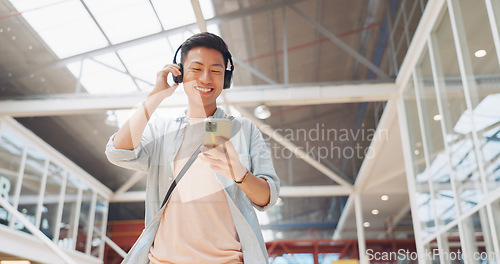 Image of Asian man, phone and headphones for listening to music and dancing while walking in creative office with smile, happiness and positive mindset. Male entrepreneur during travel with network connection