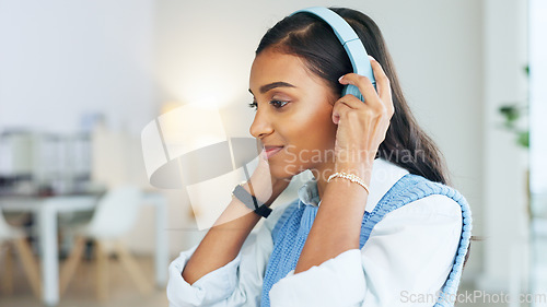 Image of Young Indian creative with headphones sitting alone in an office and smiling. Copywriter looking pleased with her works as she types. Graphic designer uses music for motivation focusing on her task