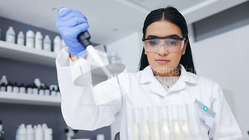 Image of Female scientist experimenting with test tubes and a syringe. One young biologist or chemist putting blue liquid in glassware for medicinal research testing at an innovative research lab or clinic