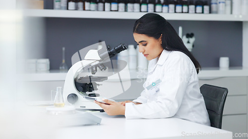 Image of Young scientist using a digital tablet and microscope in a lab. Female pathologist analyzing medical samples while doing experiments to develop a cure. Microbiologist conducting forensic research