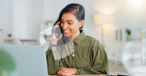 Image of Happy business woman talking on phone call or young entrepreneur answering cellphone while sitting in front of work laptop in an office. Indian female executive smiling and laughing at a funny joke.